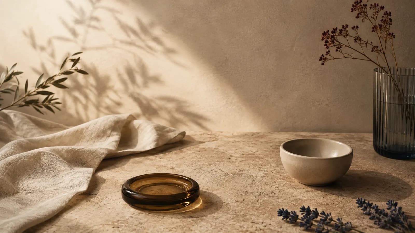 Linen, an amber dish, olive branch shadows and lavender in low sun.