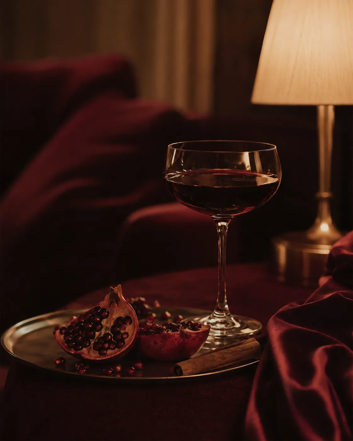A coupe glass, split pomegranate and cinnamon in lamplight.